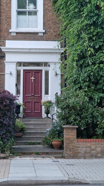 The image depicts the front entrance of a traditional brick house with a deep red wooden door featuring a brass letterbox and a gold-colored door handle. The doorway is framed by classic white archite